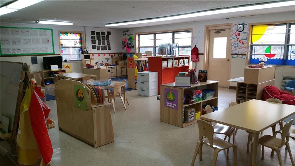 A classroom with tables, chairs, shelving units, and windows