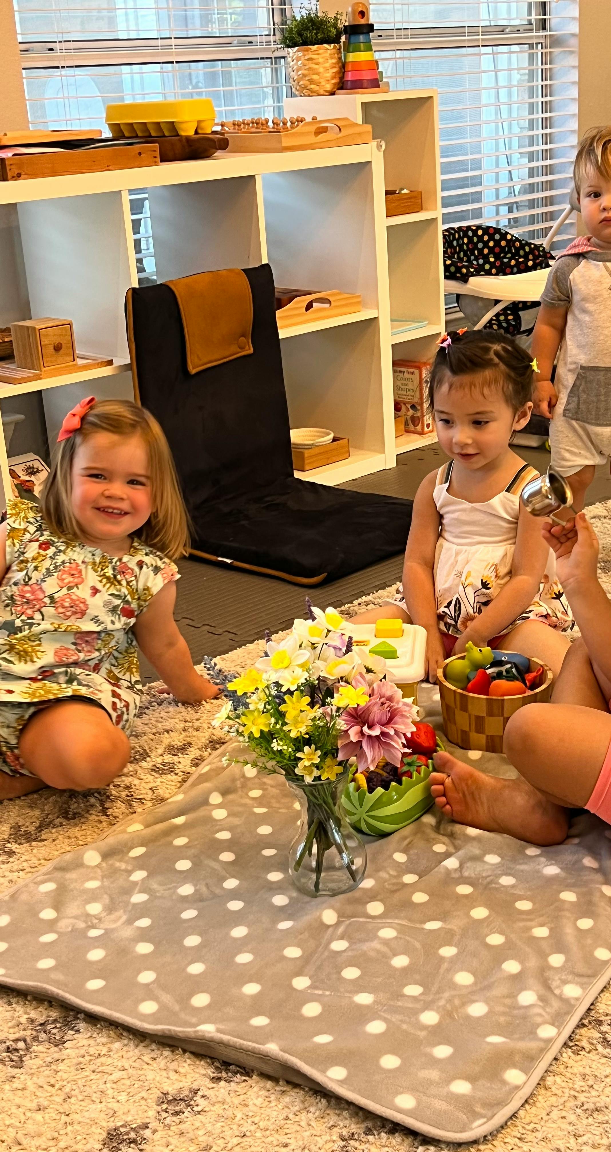 Three children sitting on a rug with flowers and toys