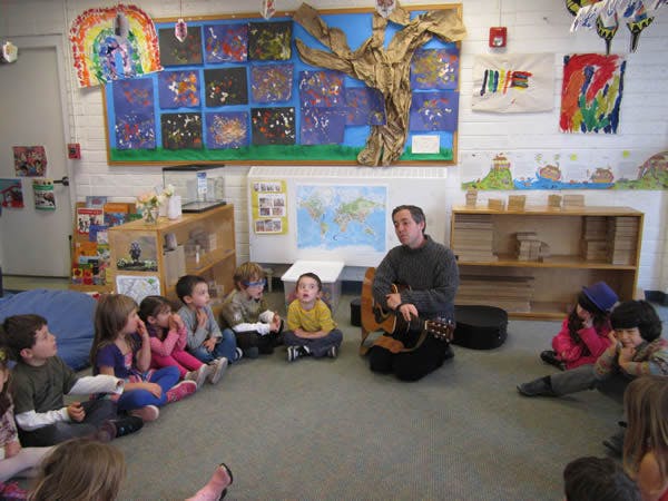 Adult playing guitar for children sitting on the floor in a classroom