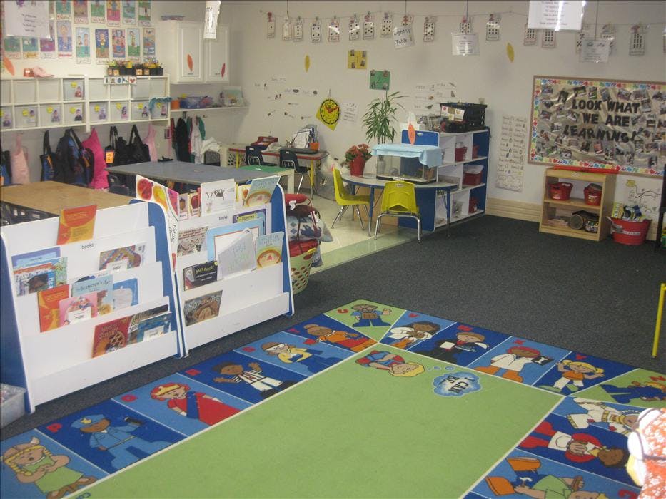 Classroom with child-sized furniture, colorful rug, book displays, and artwork on-wall decorations