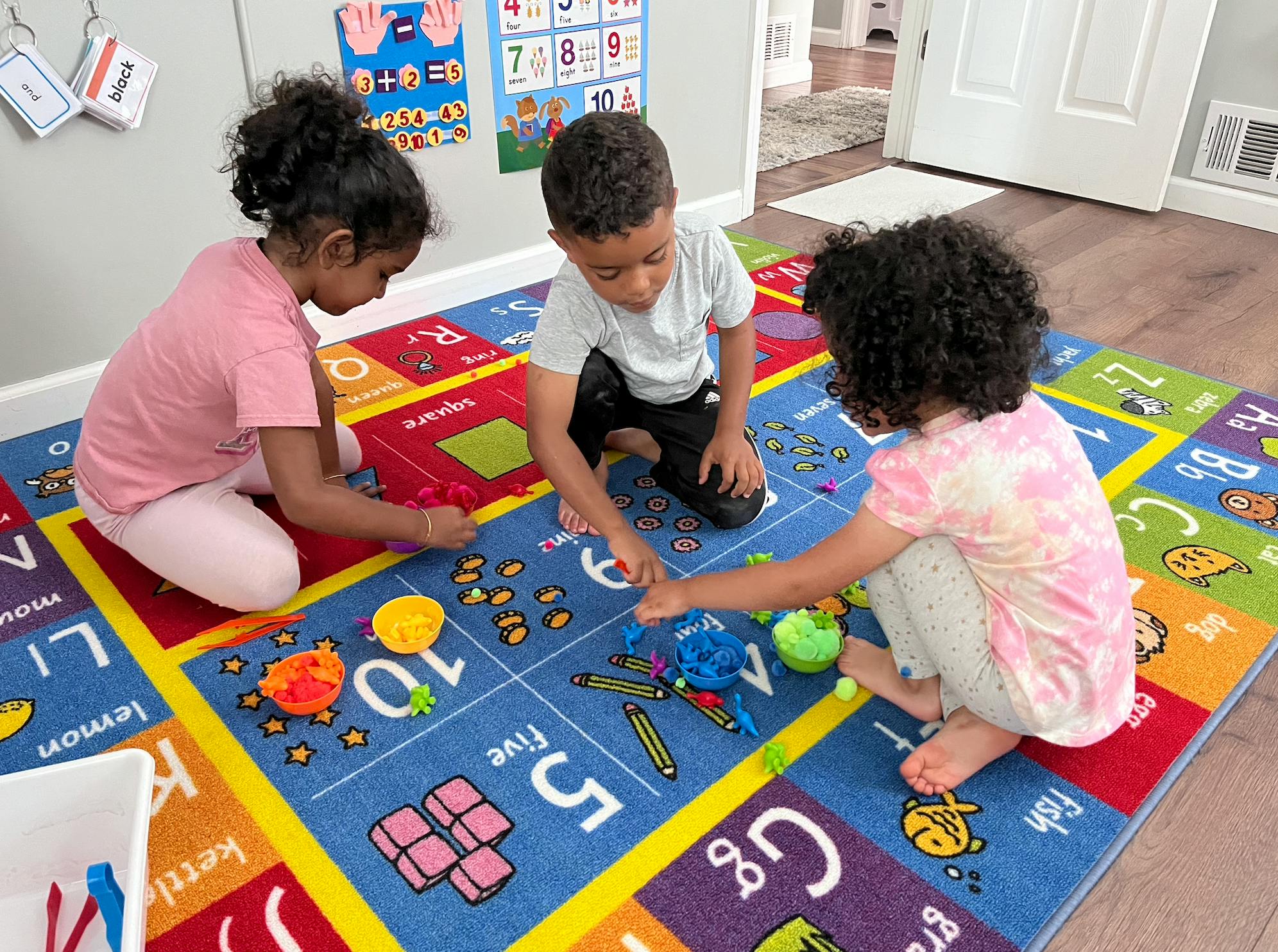 Three children playing with small objects on an alphabet rug