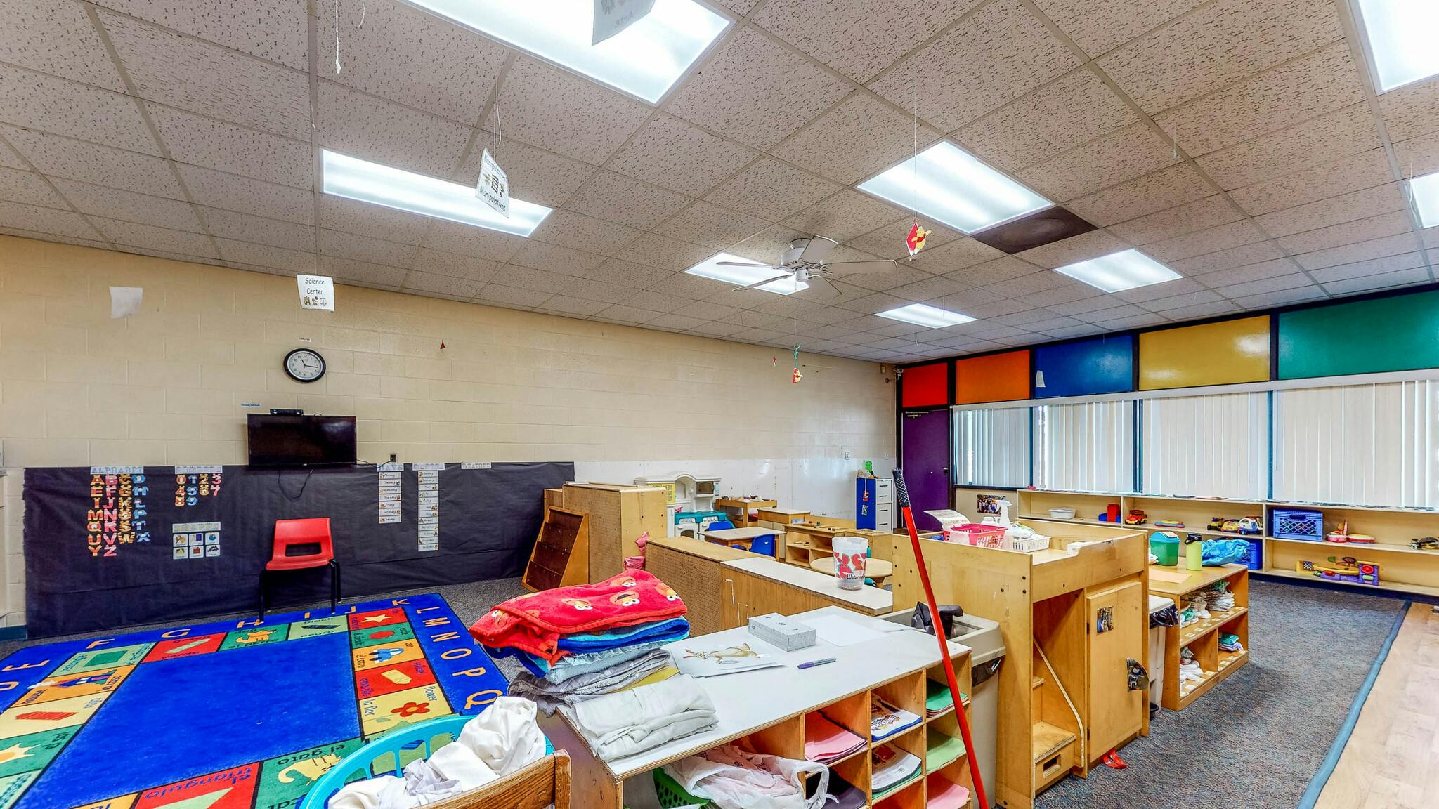 A colorful classroom with play areas, shelves, and a large alphabet rug