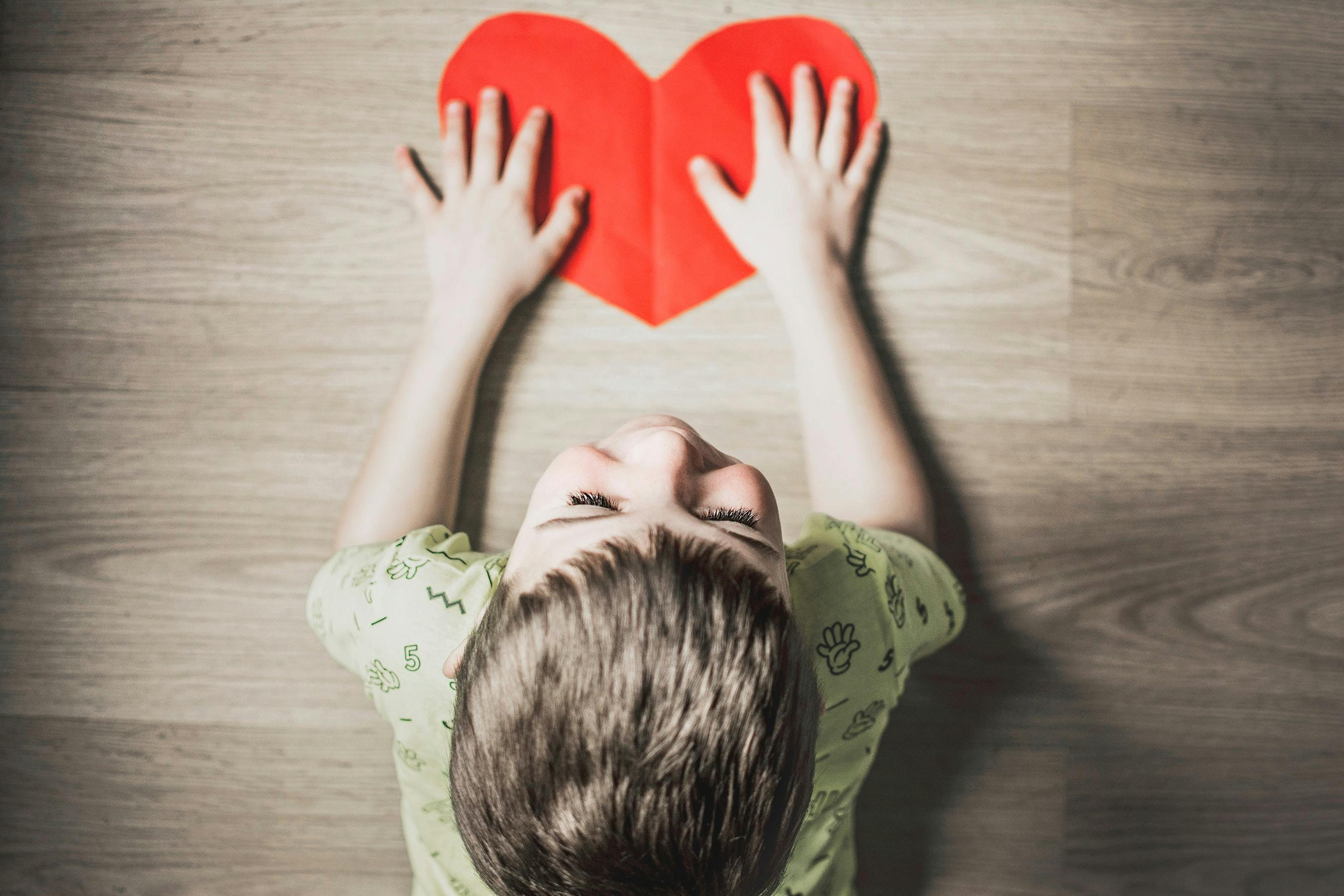 Child lying on floor with hands on a red paper heart