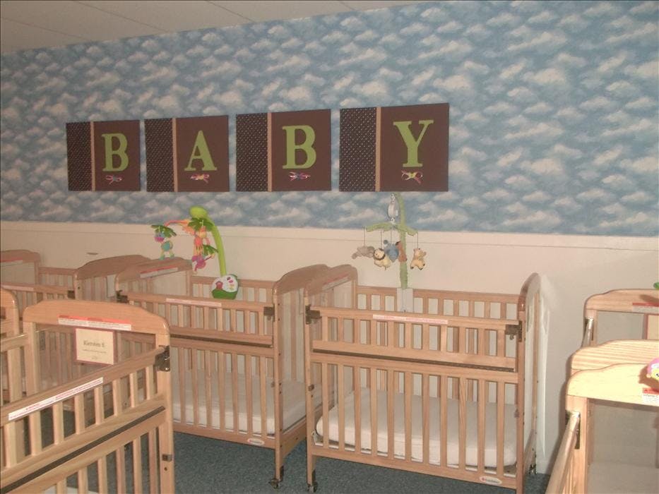 Multiple wooden cribs with mobiles in a room with \"BABY\" on the wall