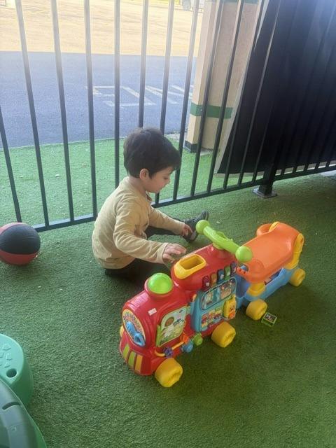 Child sitting on artificial grass playing with a toy train