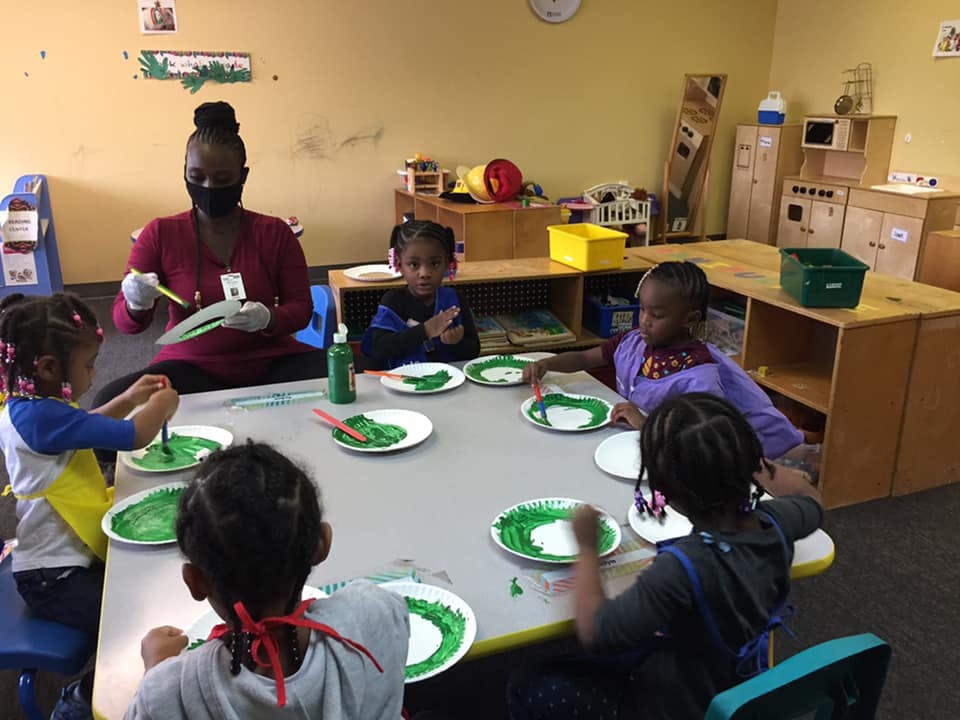 Adult and children painting at a table in a classroom