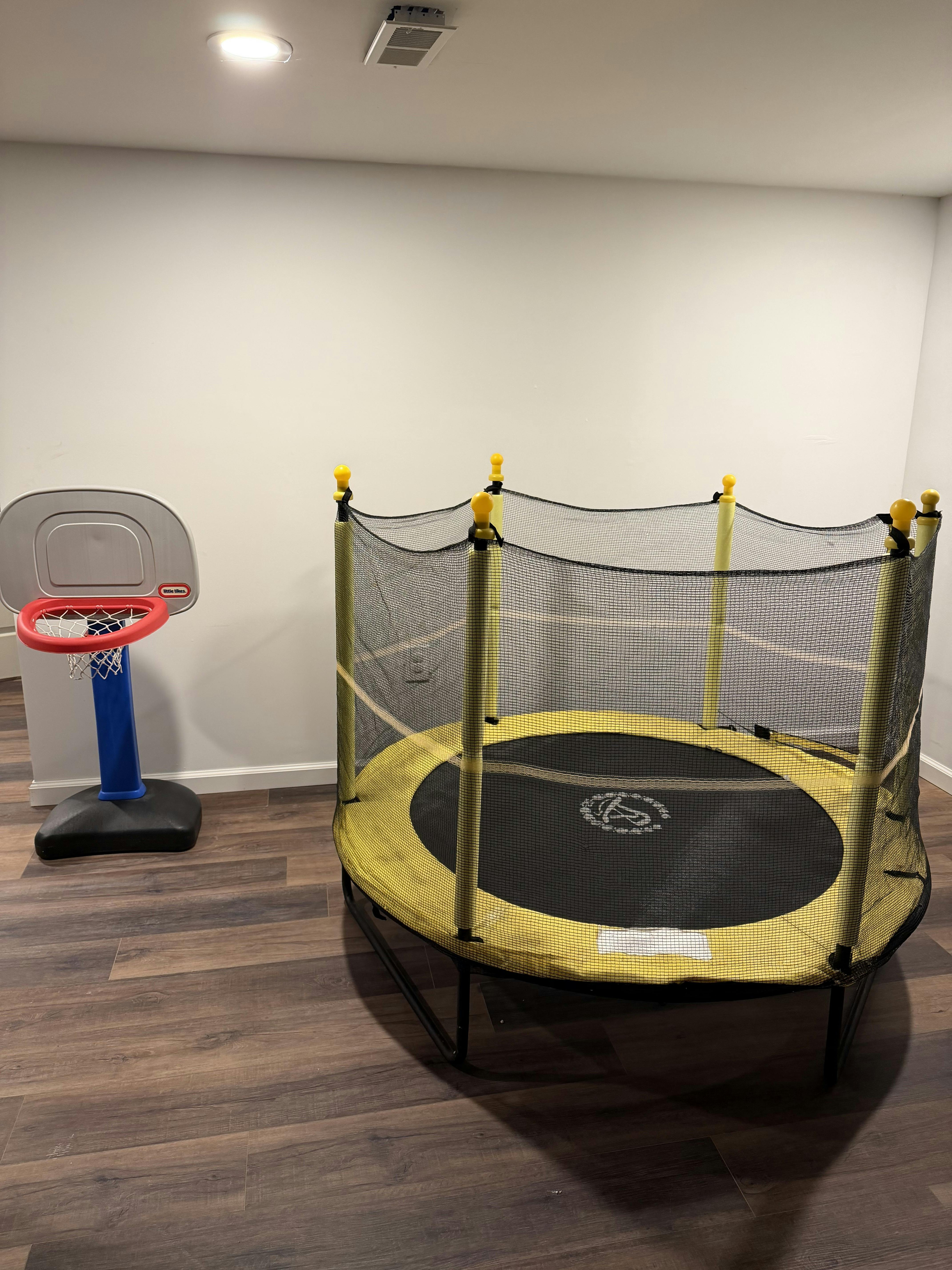Small trampoline with a safety net next to a toy basketball hoop