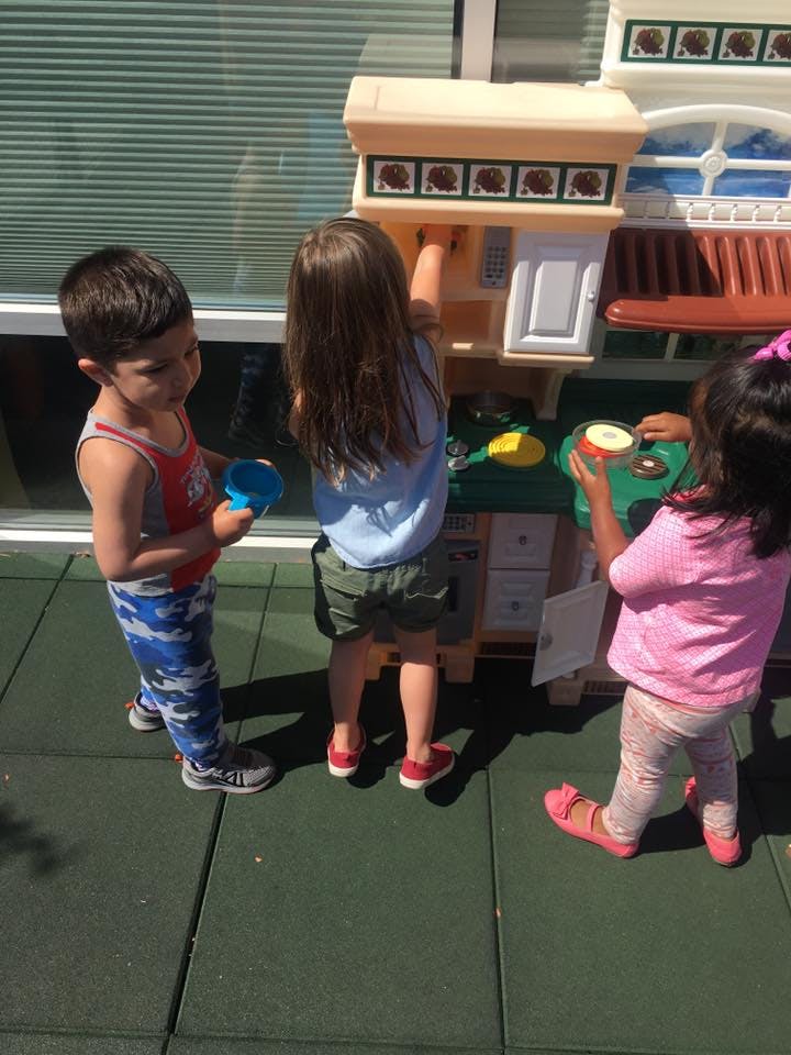 Three children playing with a toy kitchen set outdoors