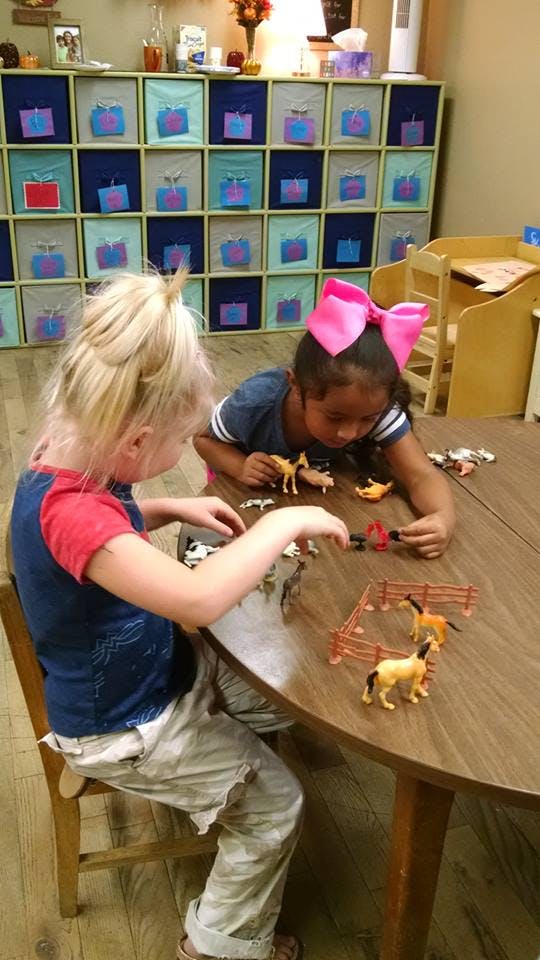 Two children playing with toy horses and fences at a table