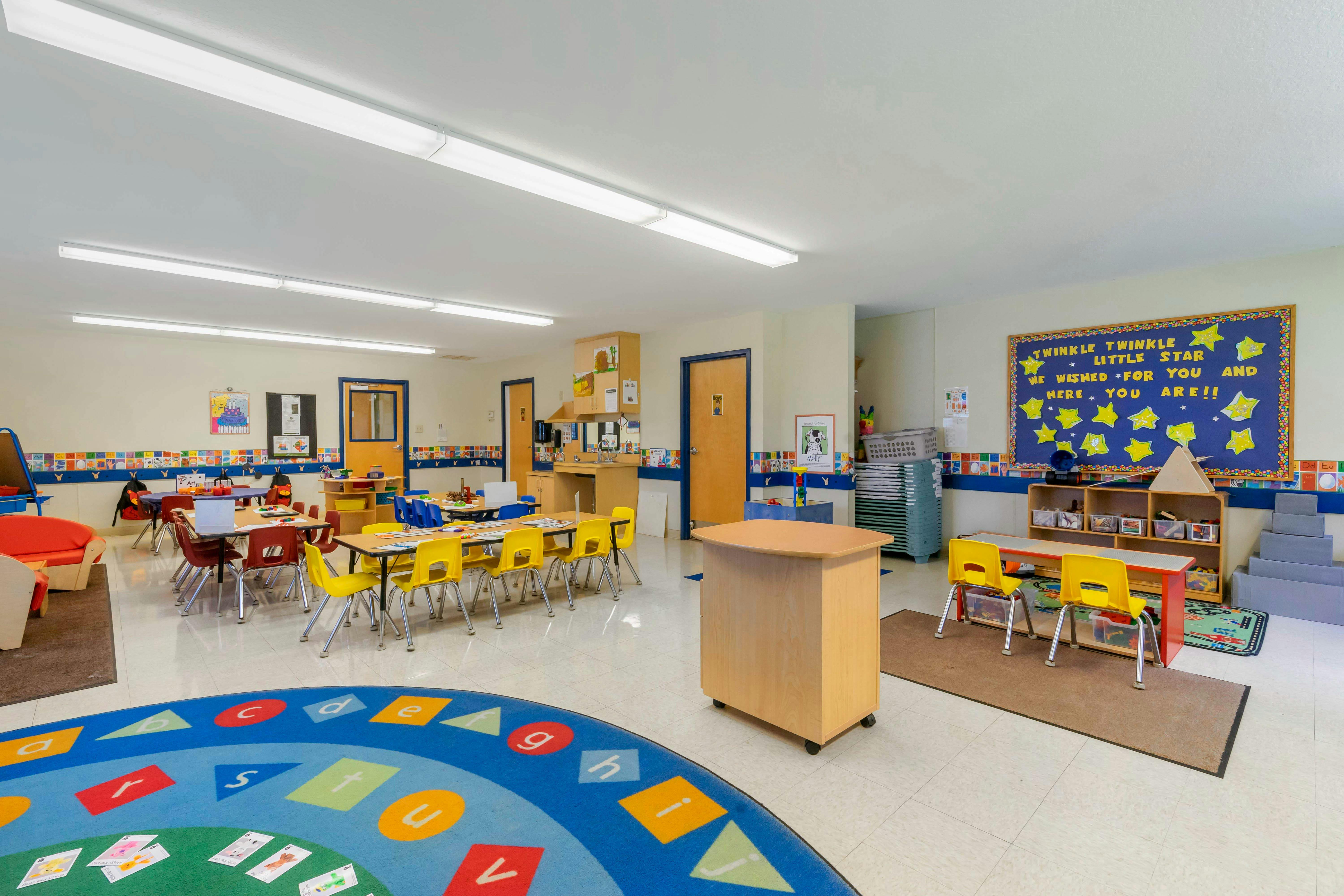 A colorful empty classroom with tables, chairs, and play areas