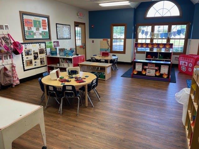 empty preschool classroom with tables, chairs, and play areas