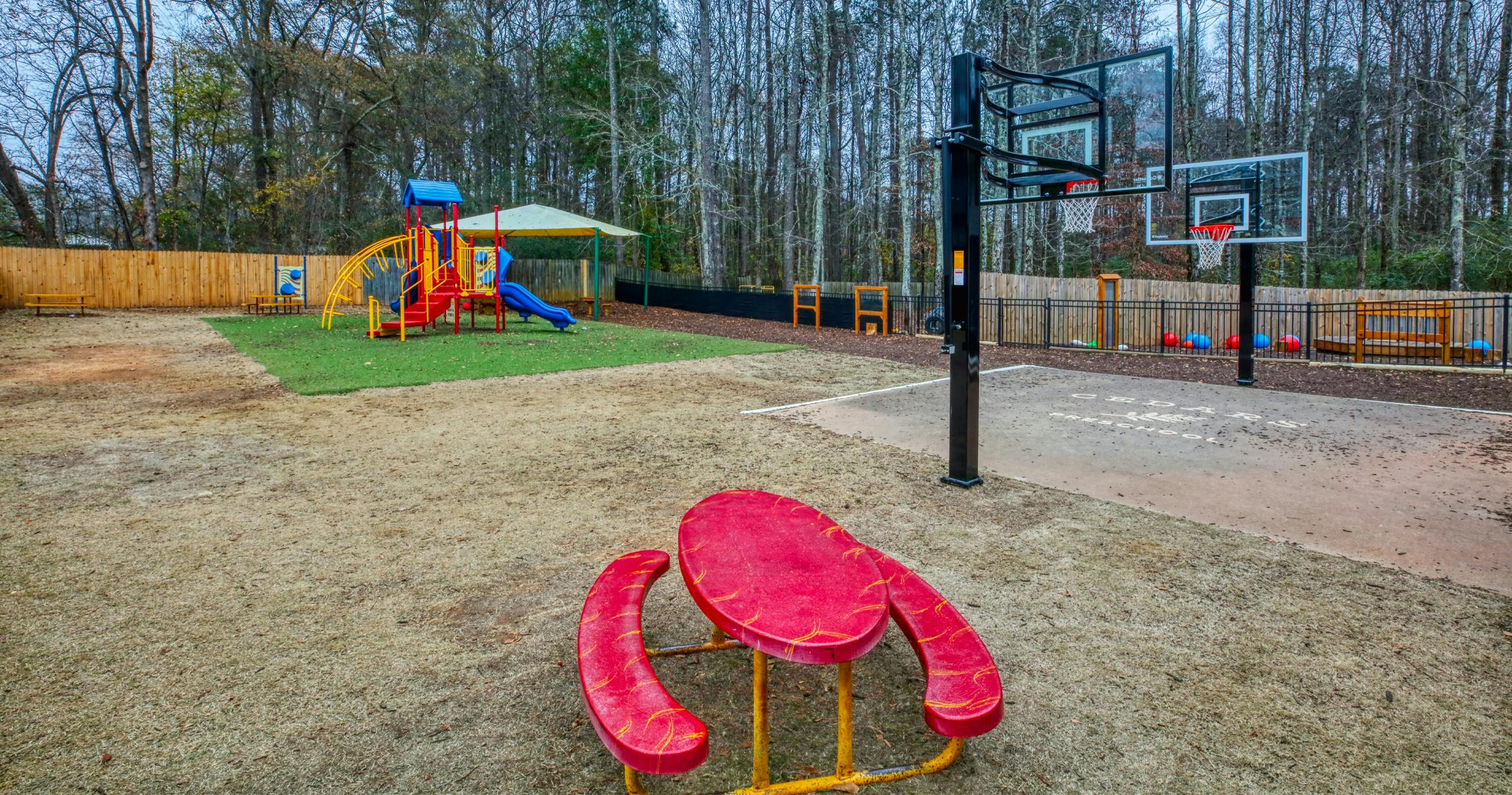 Outdoor playground with slides, swings, basketball court, and red picnic table