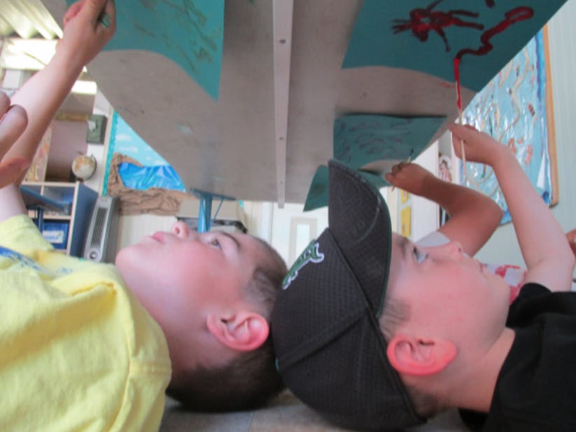 Two children lying on their backs looking up at papers under a table