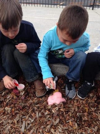 Two children doing a science experiment with pink foam on wood chips