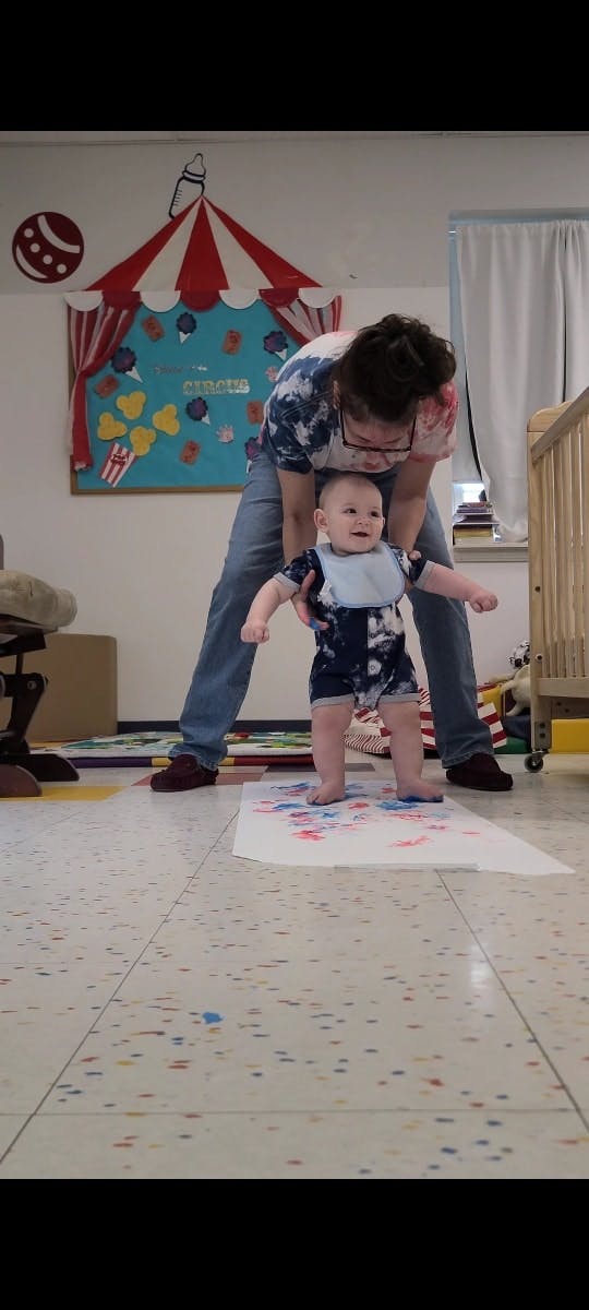 Person helping a child stand on a paper with paint on the floor