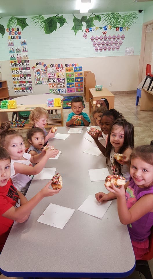 Children sitting at a table holding donuts in a classroom