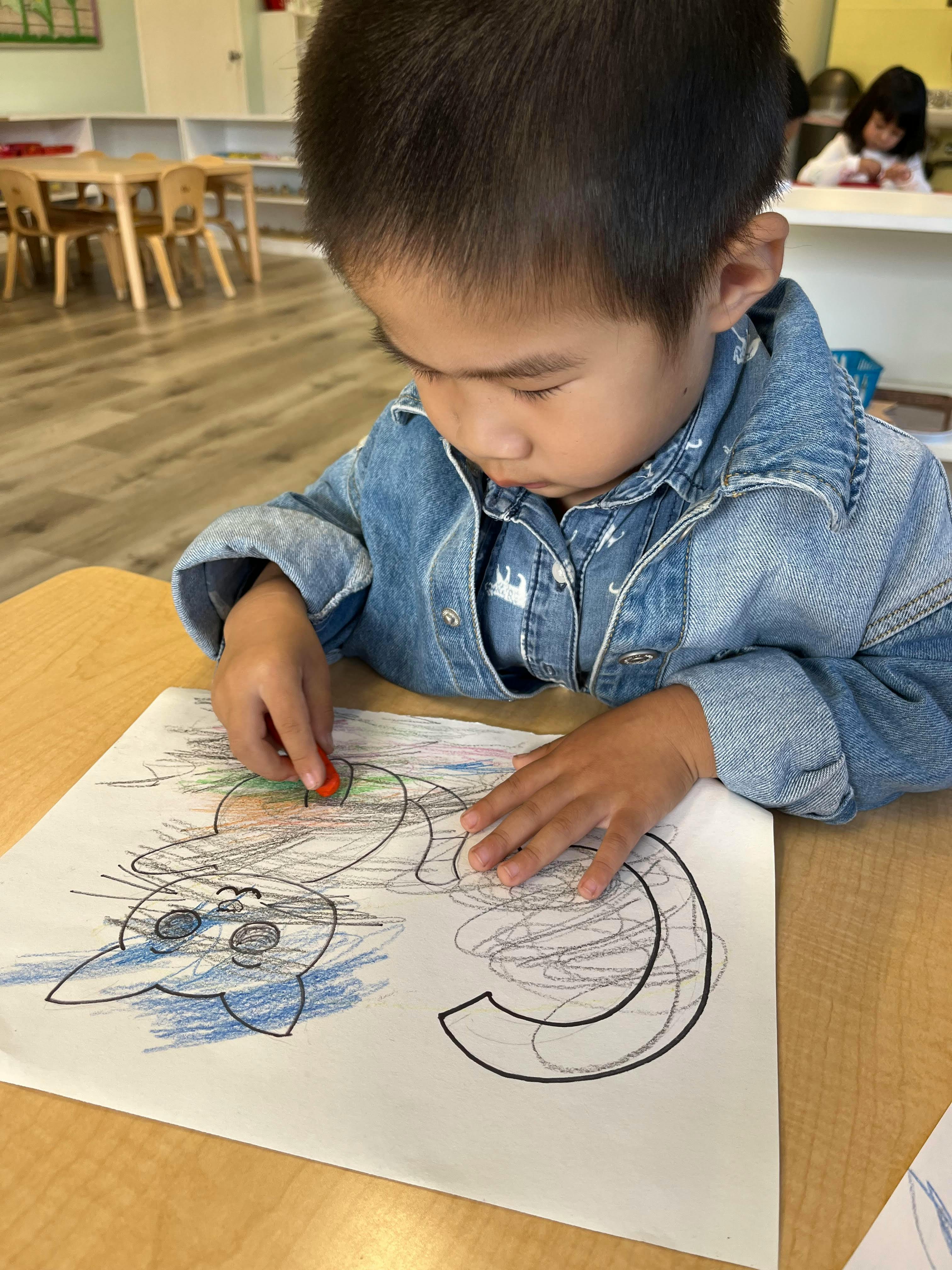 Child coloring a drawing on a table in a classroom