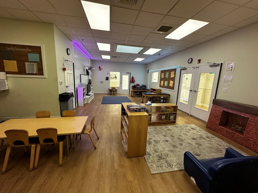 Empty classroom with small tables and chairs, a play fireplace, and a rug