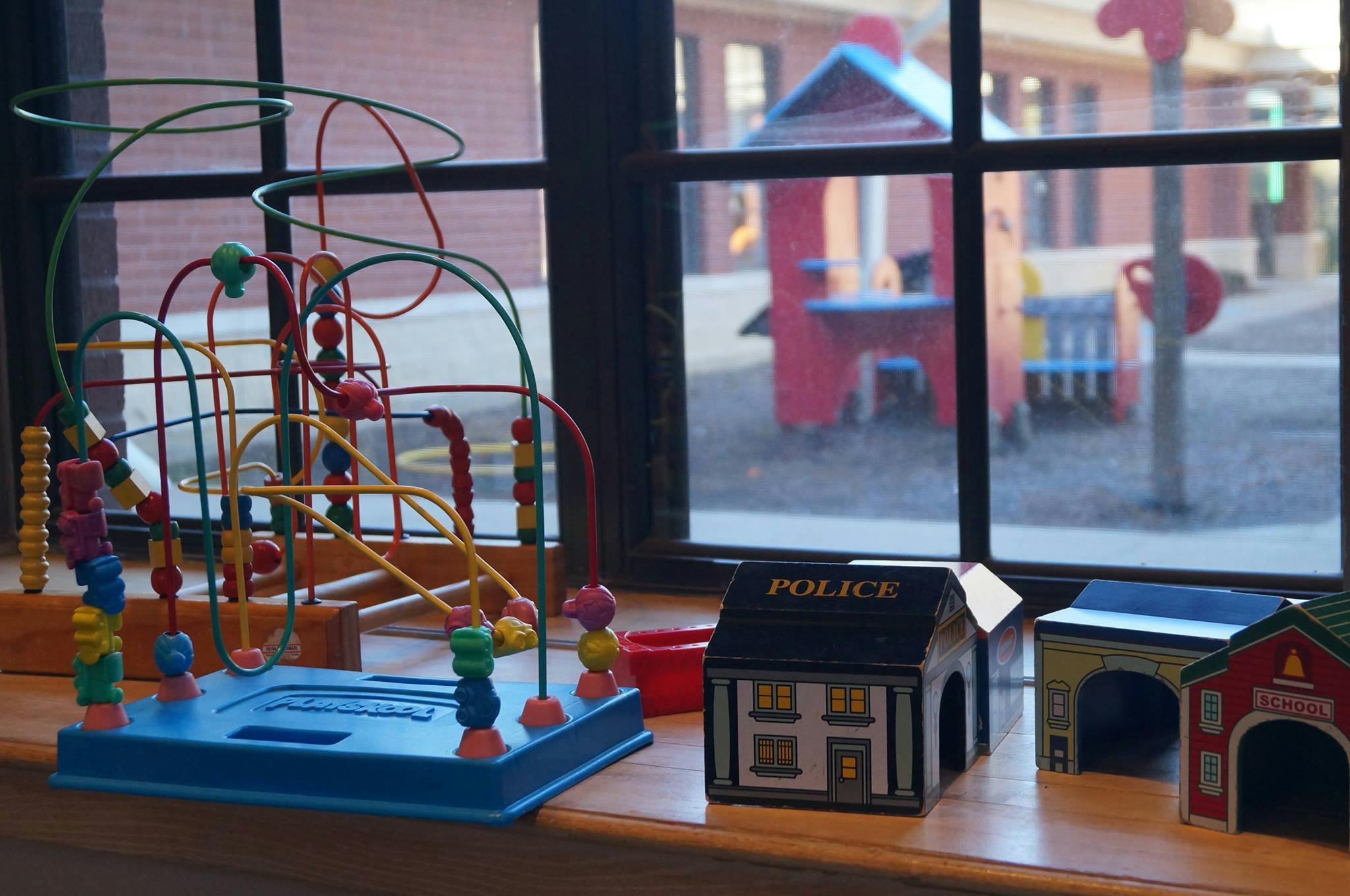 Bead maze toy and toy buildings on a windowsill with a playground outside