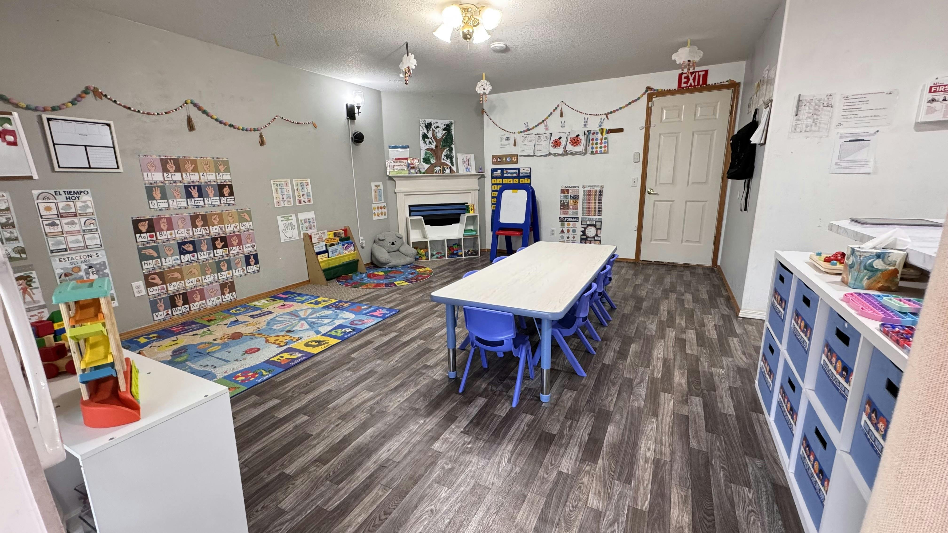 Classroom with small tables and chairs, shelves with books, and a colorful rug