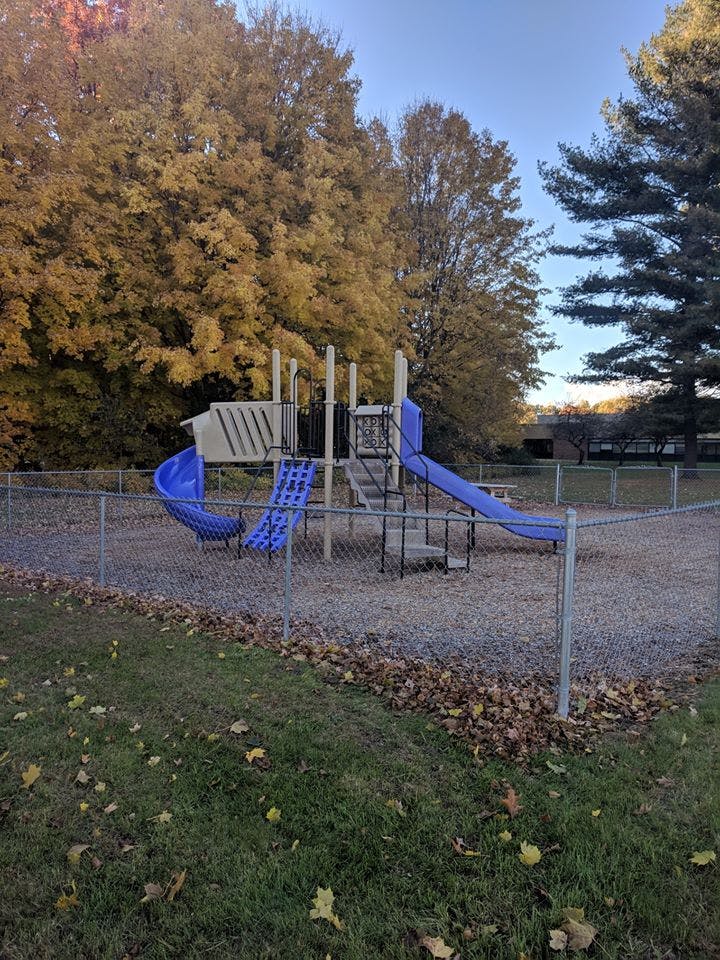 Playground with blue slides and climbing structures behind a chain-link fence
