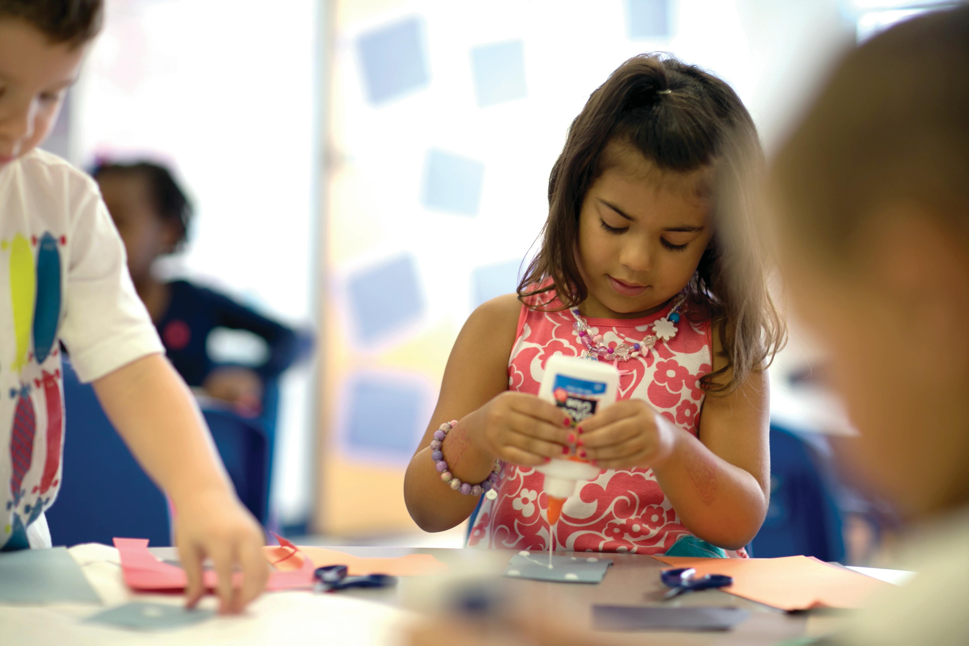 Child holding a glue bottle at a table