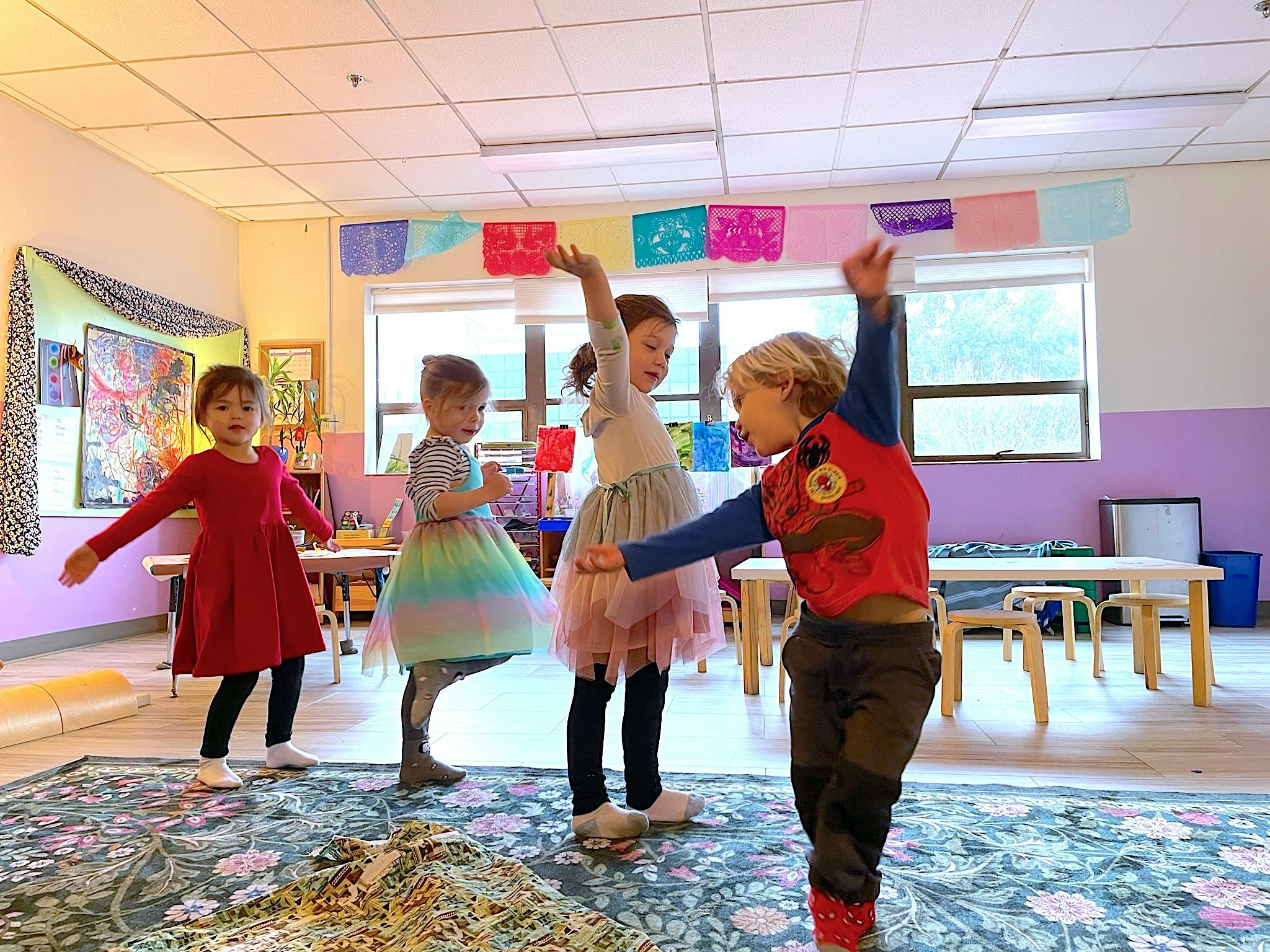 Four children dancing with arms raised in a classroom