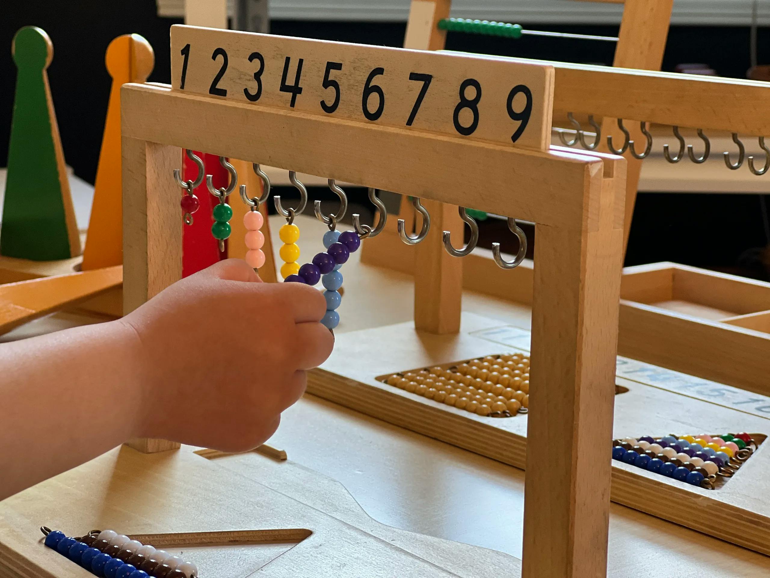 Child's hand holding a string of beads on a wooden counting frame