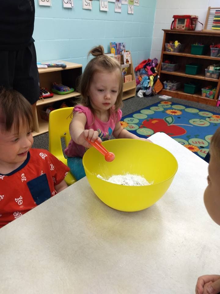 Child stirring white powder in a yellow bowl at a table