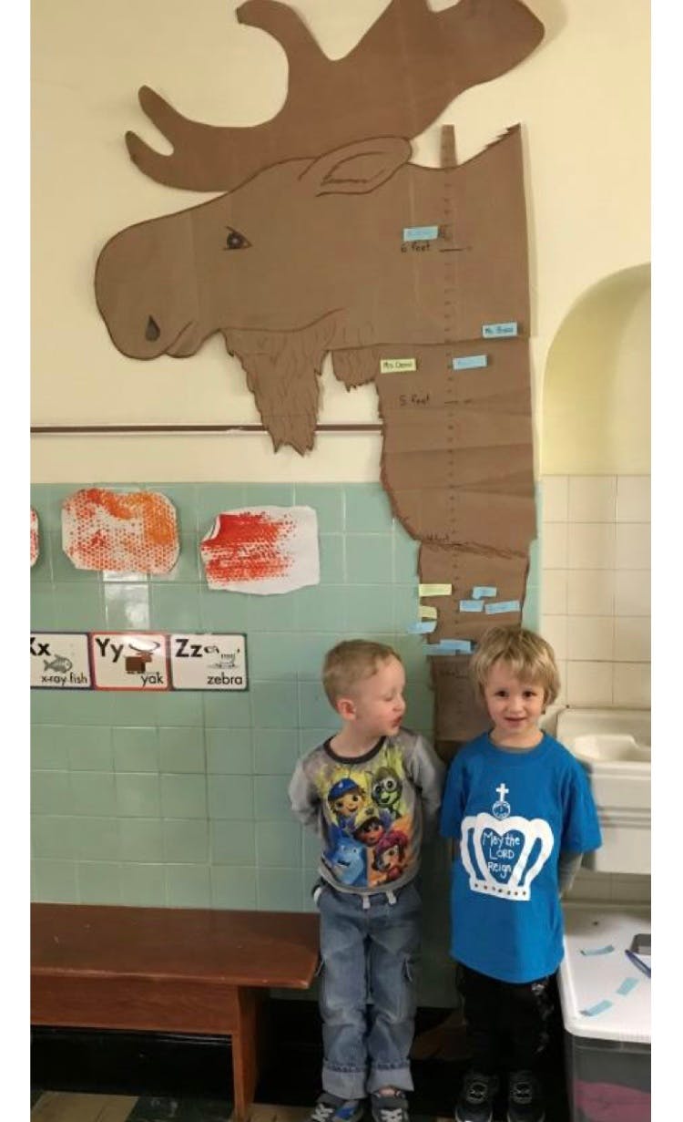 Two children standing in front of a large cardboard moose cutout