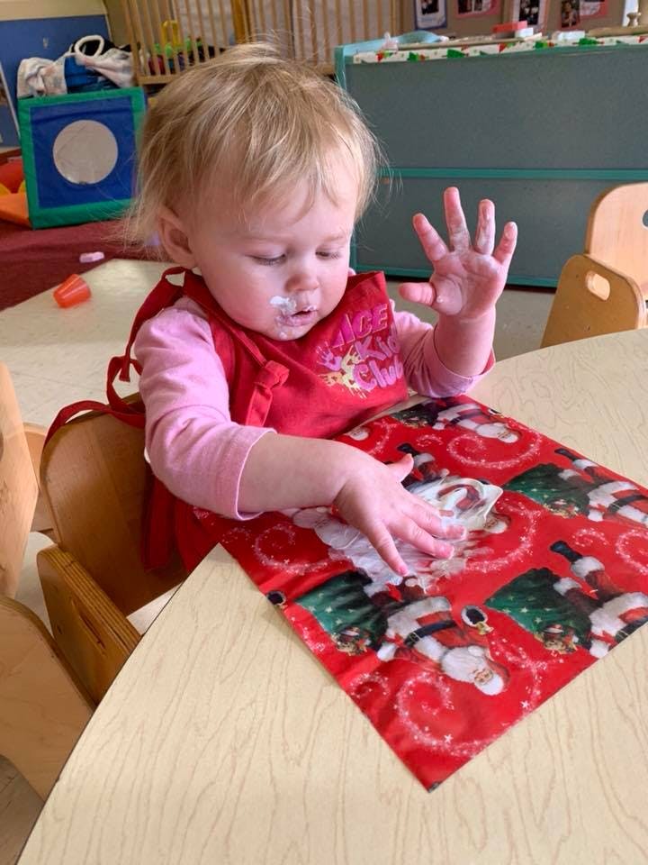 Child in a high chair with a bib, touching a red placemat