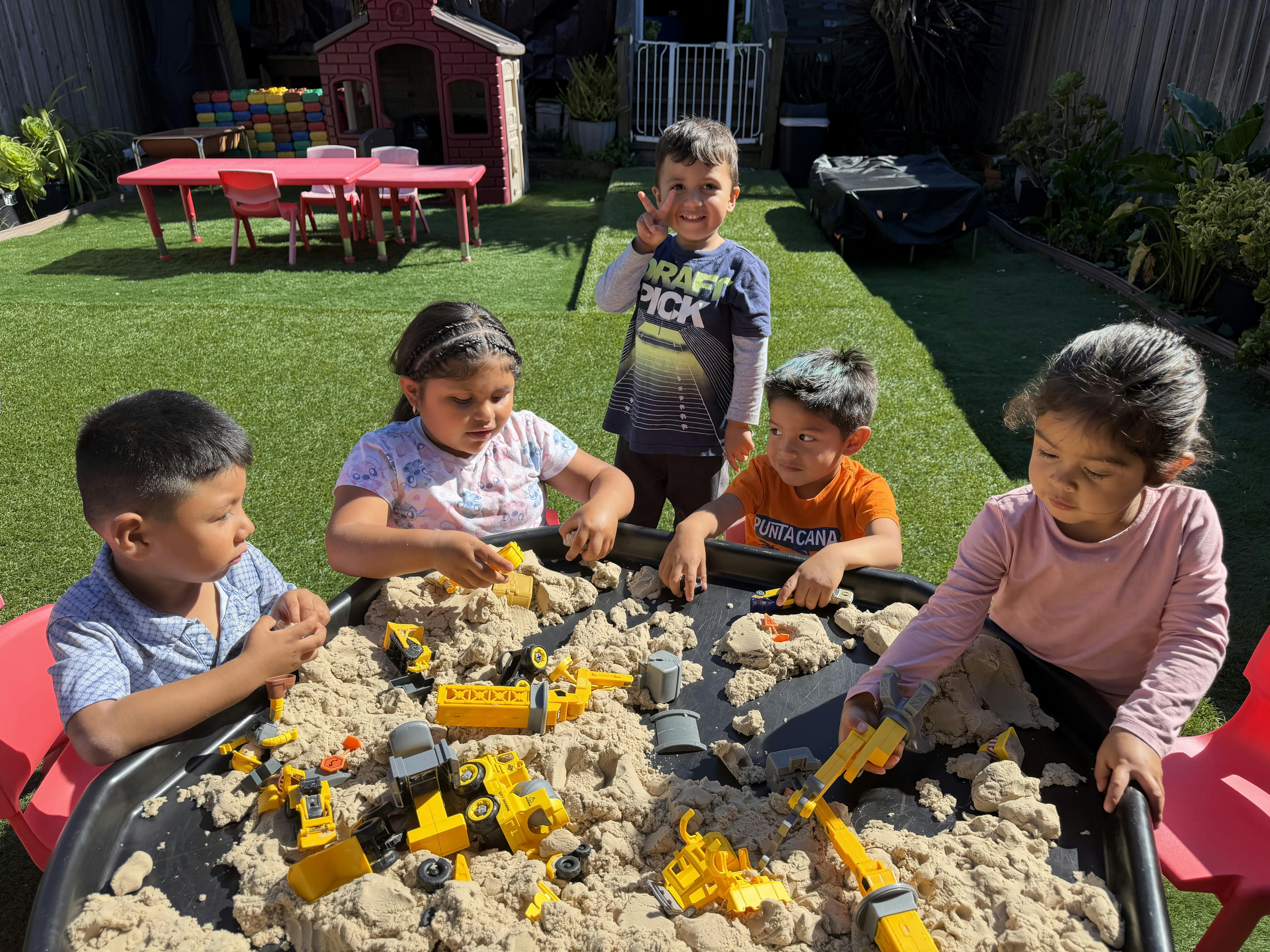 Group of children playing with toy construction vehicles in a large sand tray