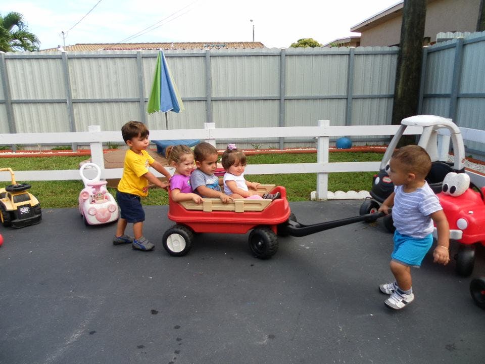 Children playing with a red wagon, one pulling and another pushing