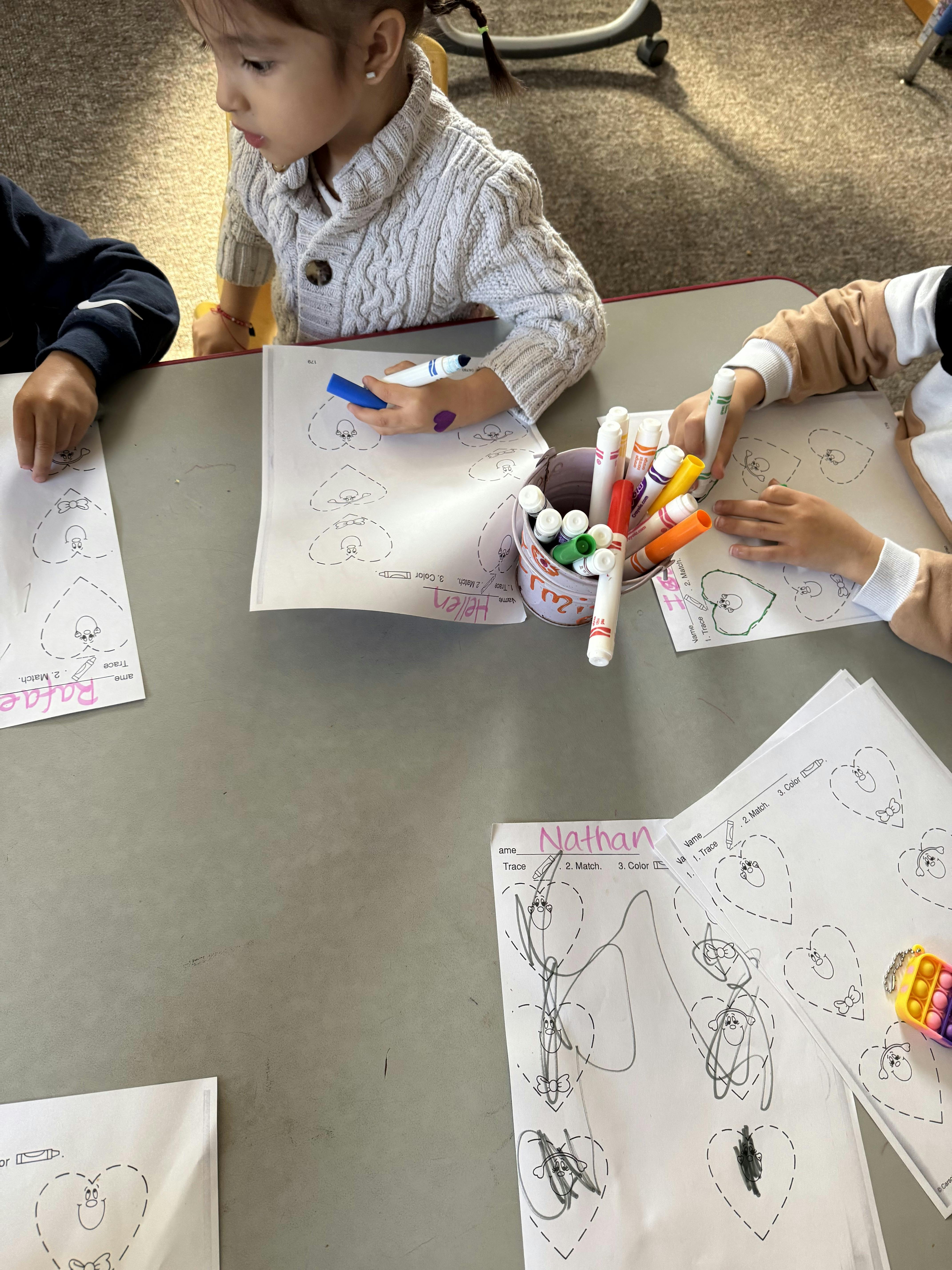Children sitting at a table tracing heart shapes from a worksheet
