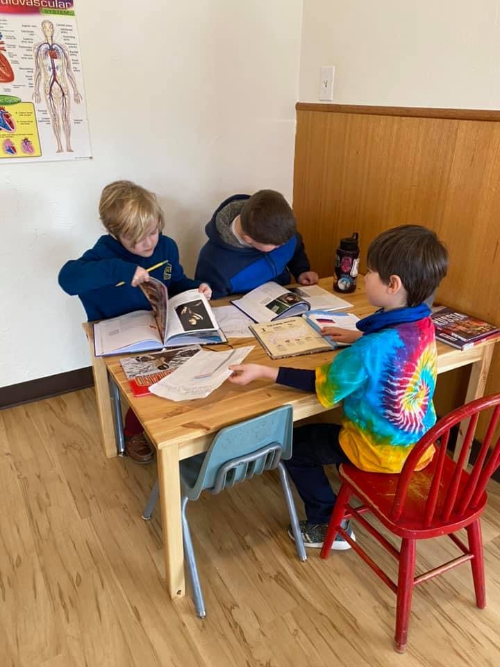 Three children reading books at a table