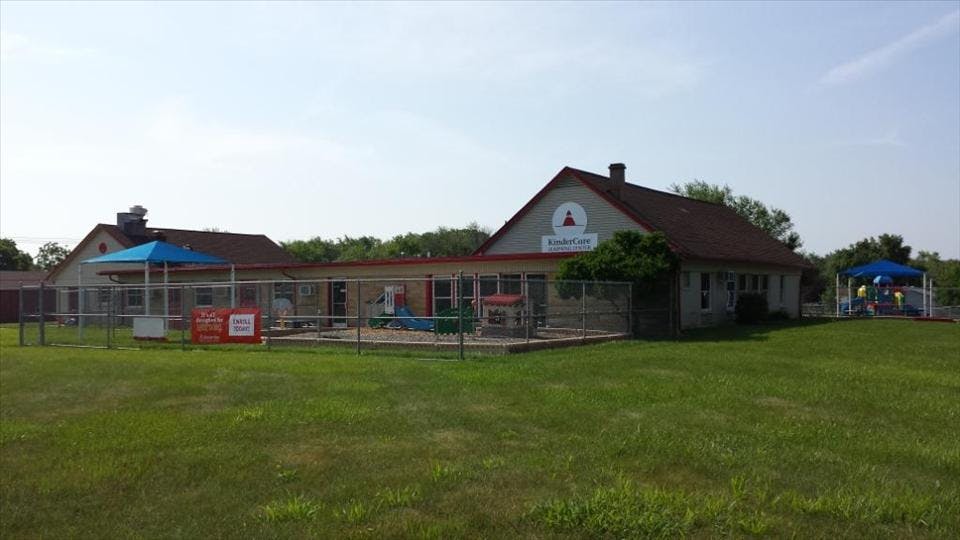 KinderCare building with a fenced playground and a sign that reads "Enroll Today"