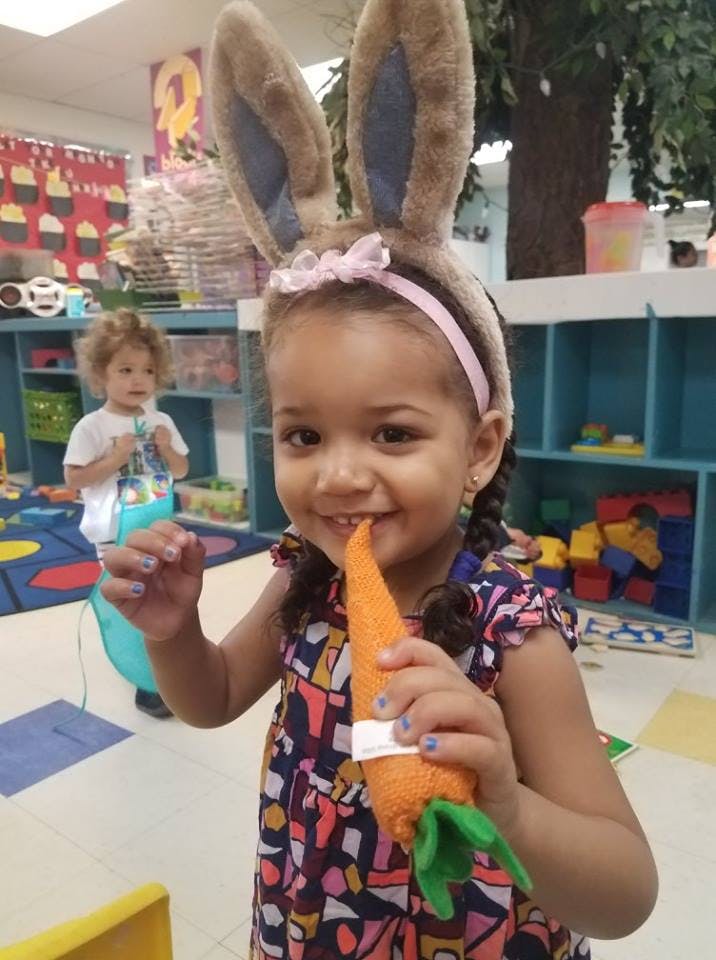 Child wearing bunny ears and holding a toy carrot in a classroom