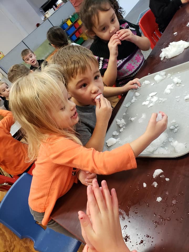 Children playing with snow on a tray at a table