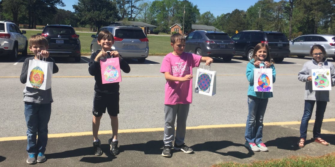 Five children holding up colorful drawings outdoors