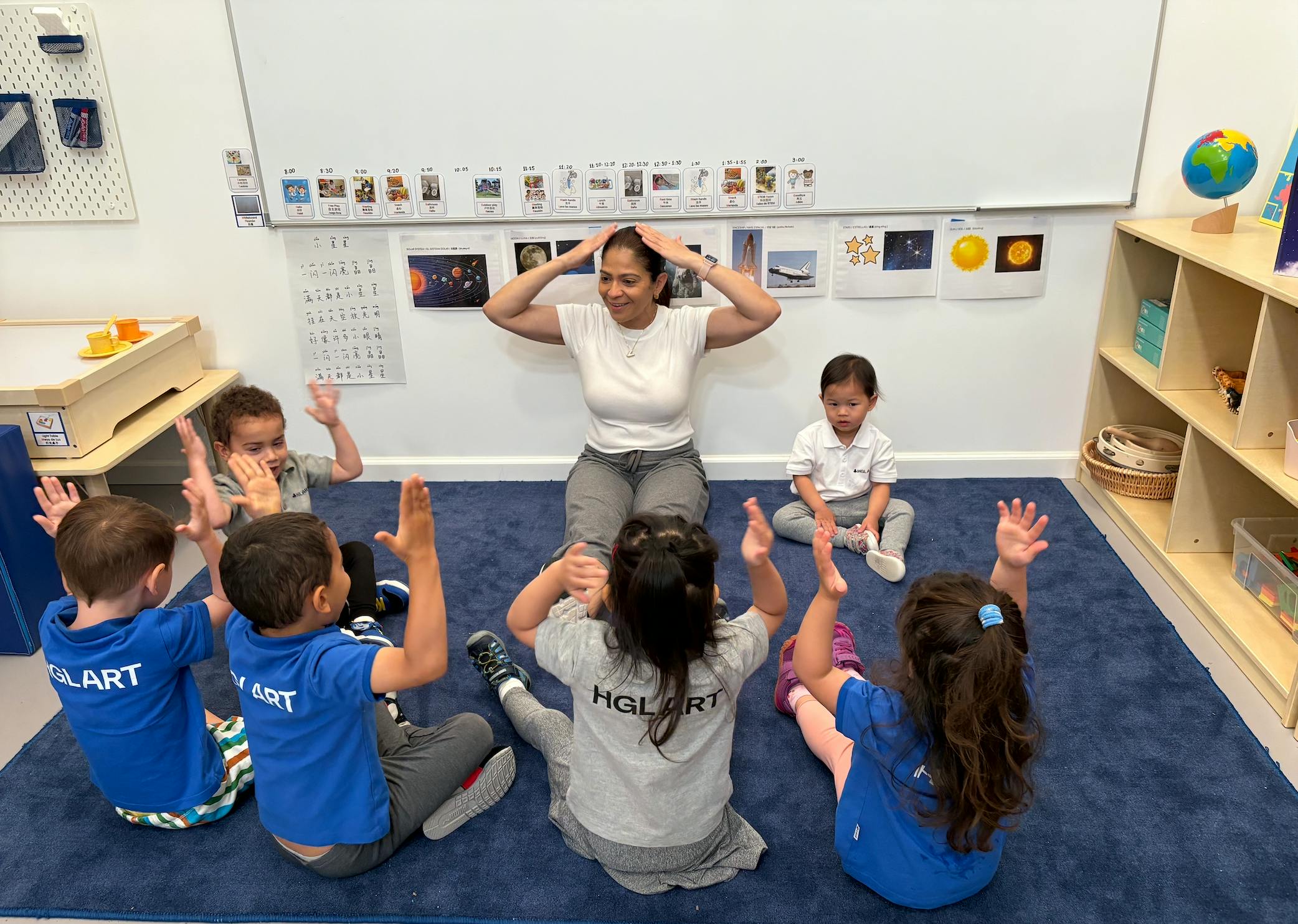 Adult and children sitting on floor with hands raised in a classroom