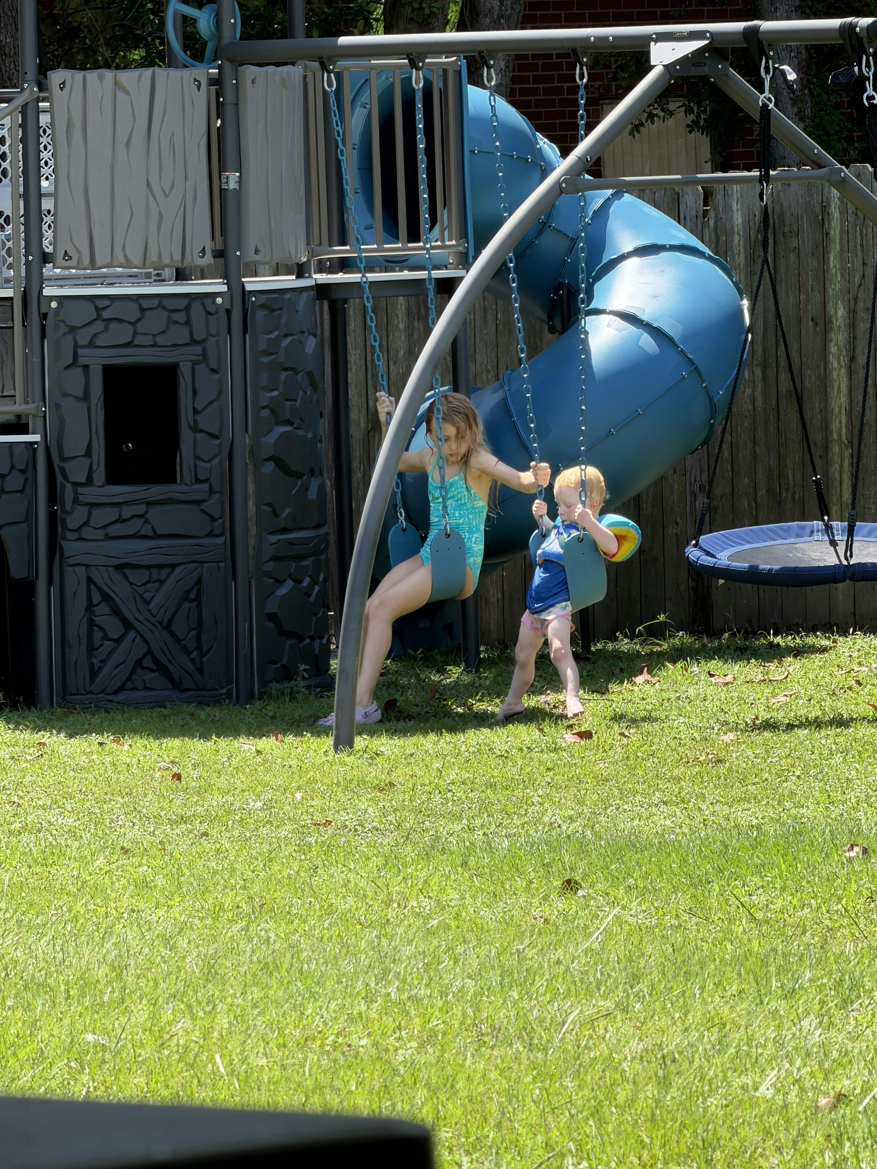 Two children playing on a backyard swing set