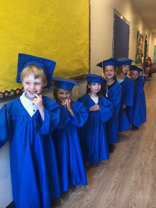 Children in blue graduation caps and gowns standing in a line