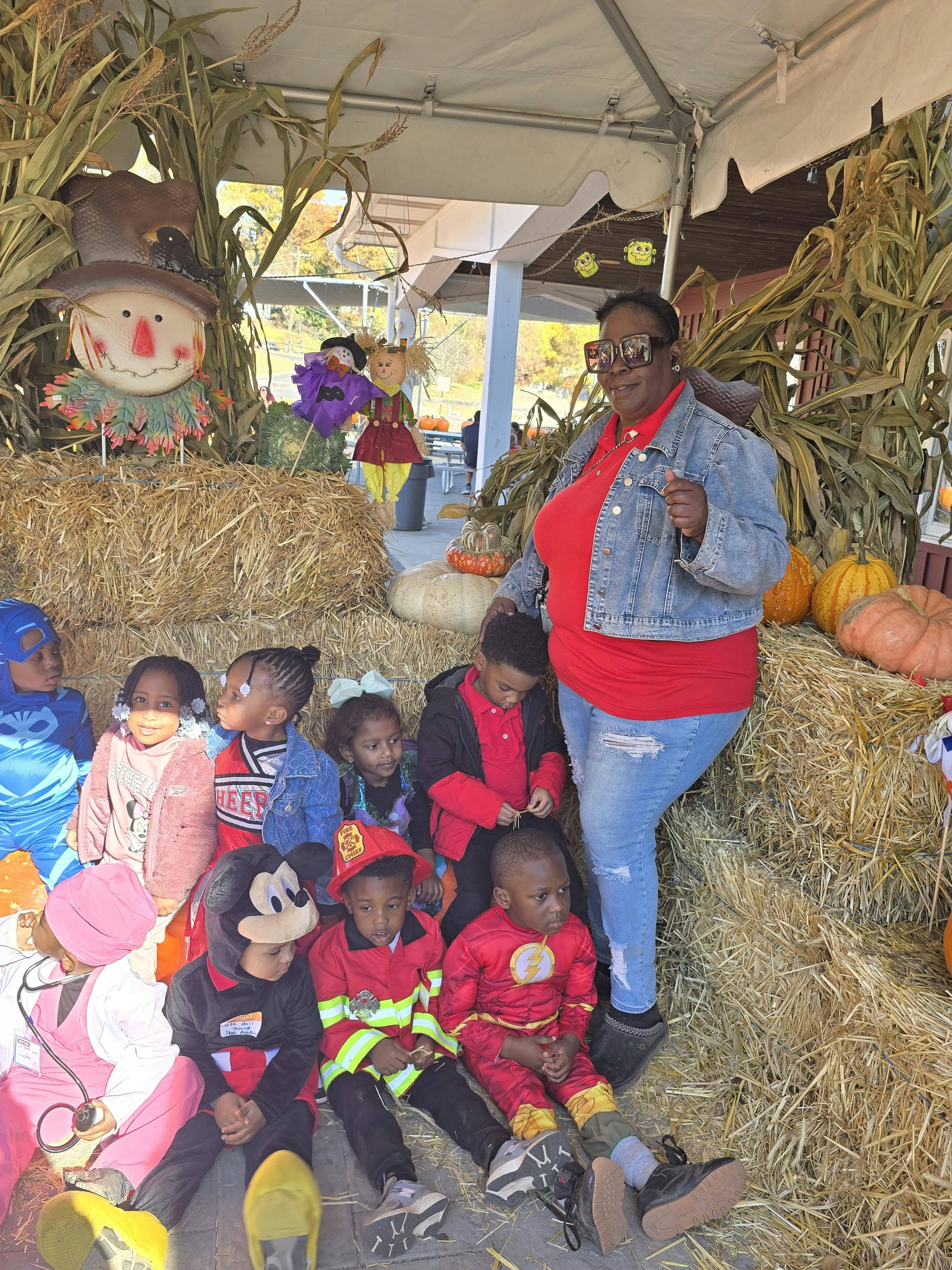 Group of children in costumes and an adult posing in front of fall decorations