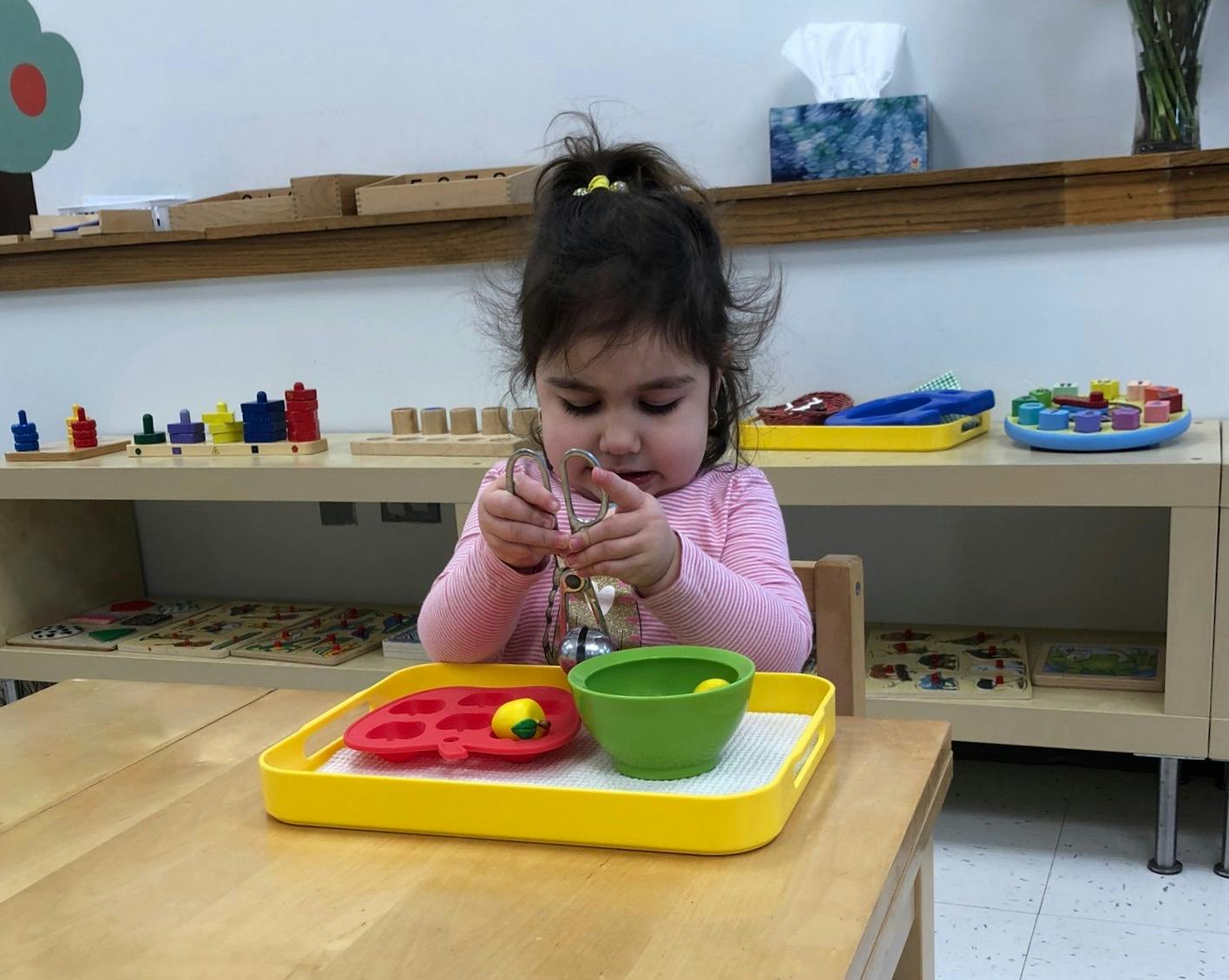 Child playing with small objects on a tray at a table