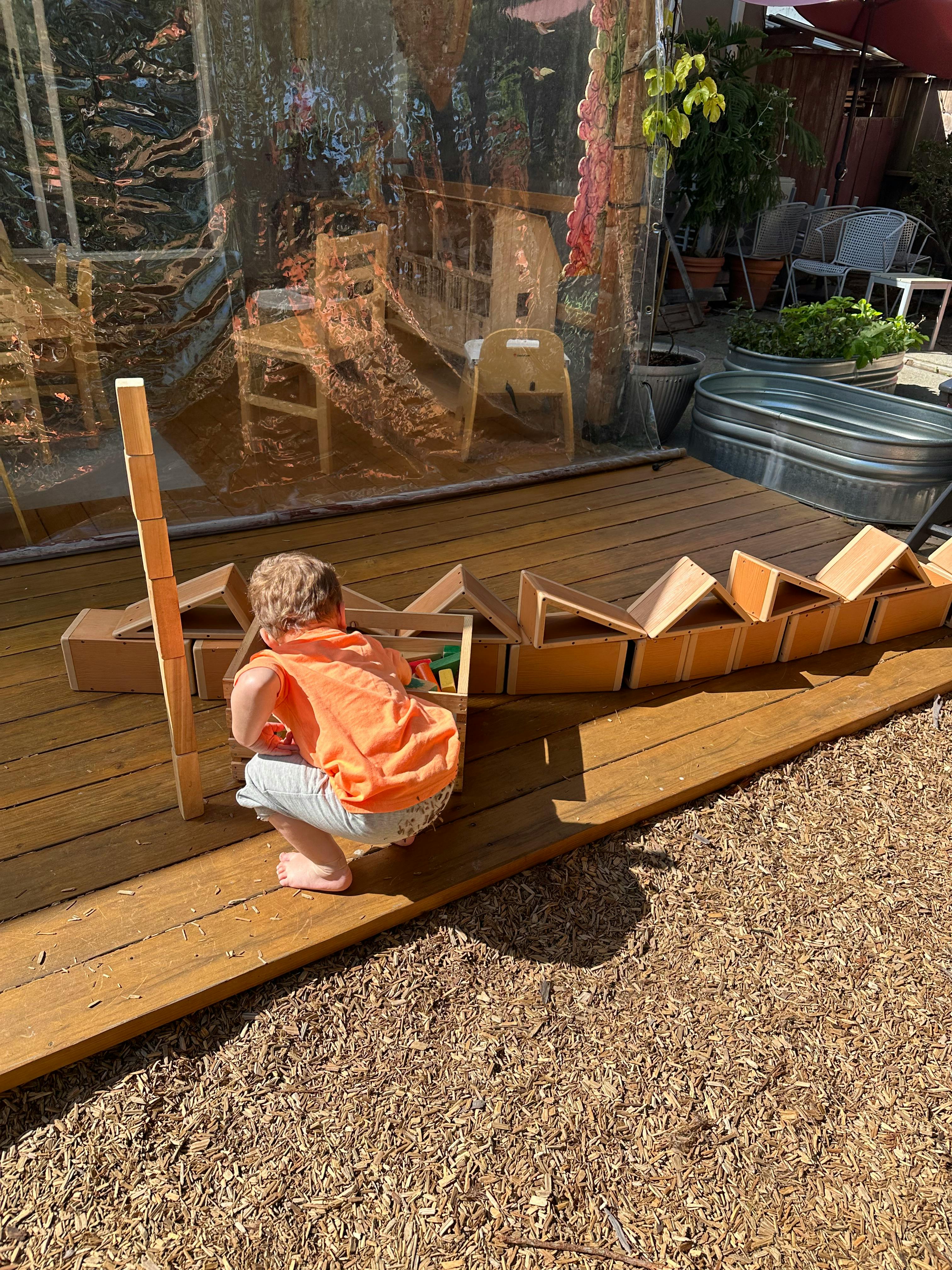 Child crouching and playing with wooden blocks on a deck