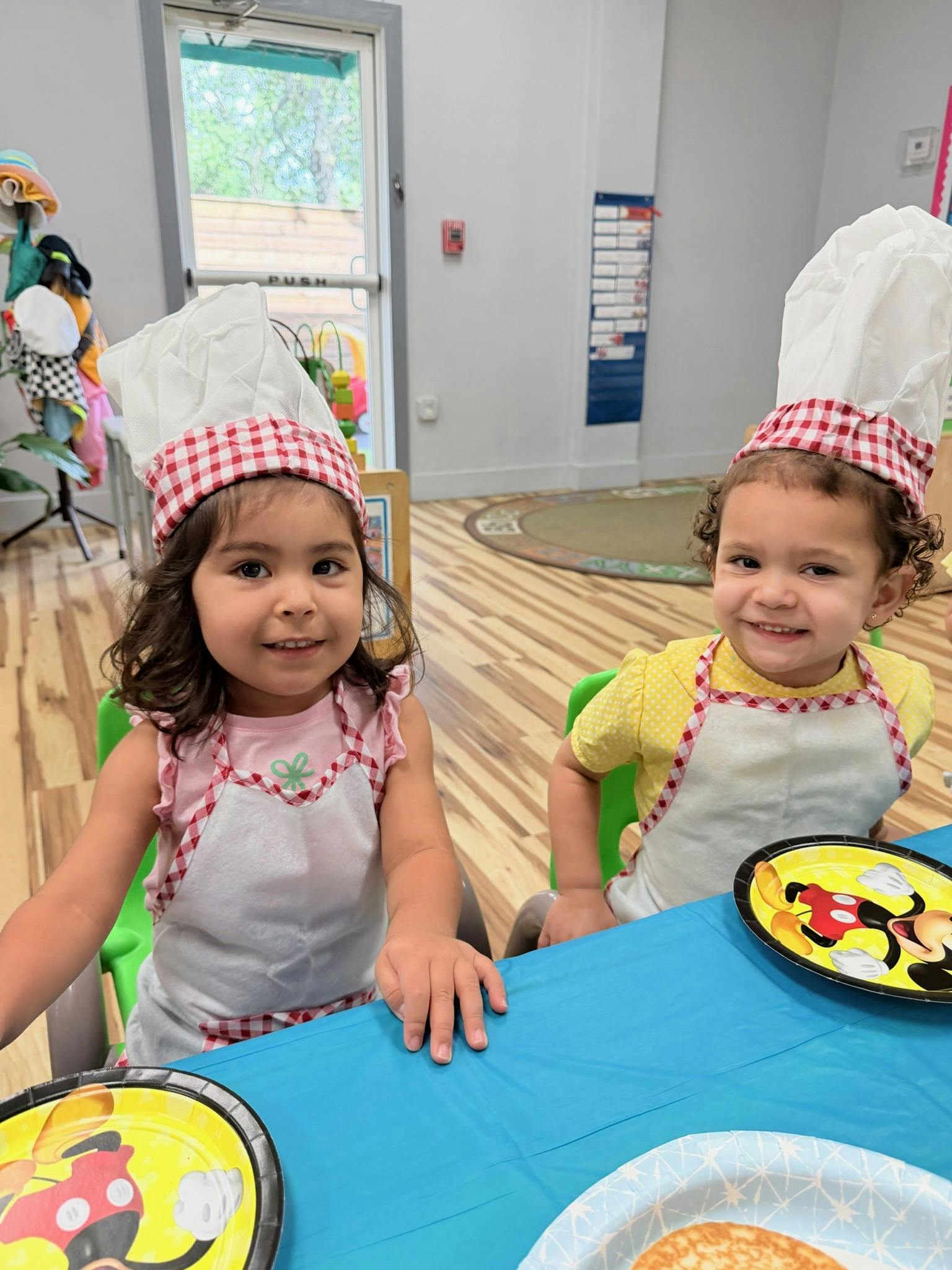 Two children wearing chef hats and aprons sitting at a table