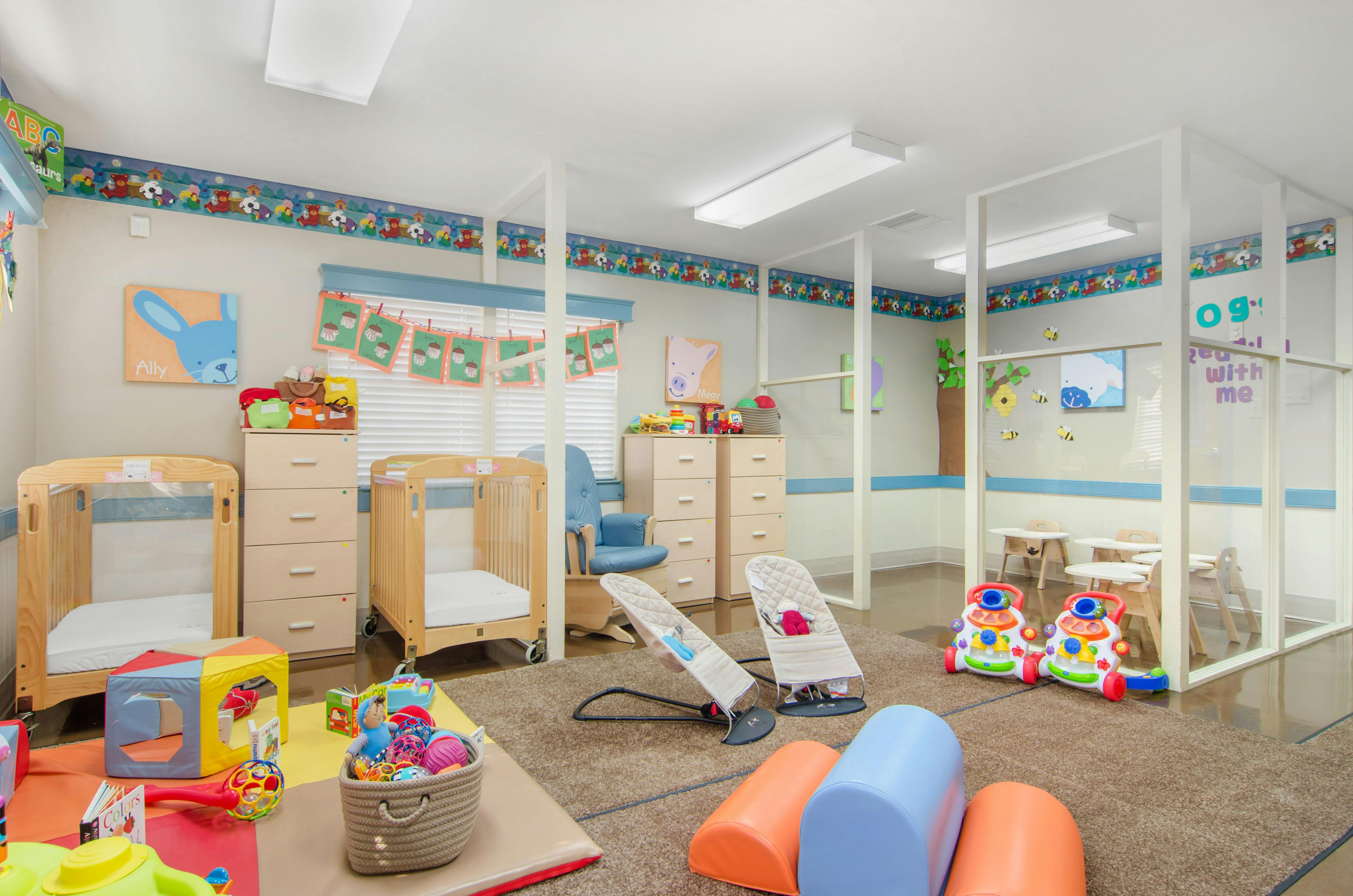 A colorful childcare classroom with cribs, play mats, and baby equipment