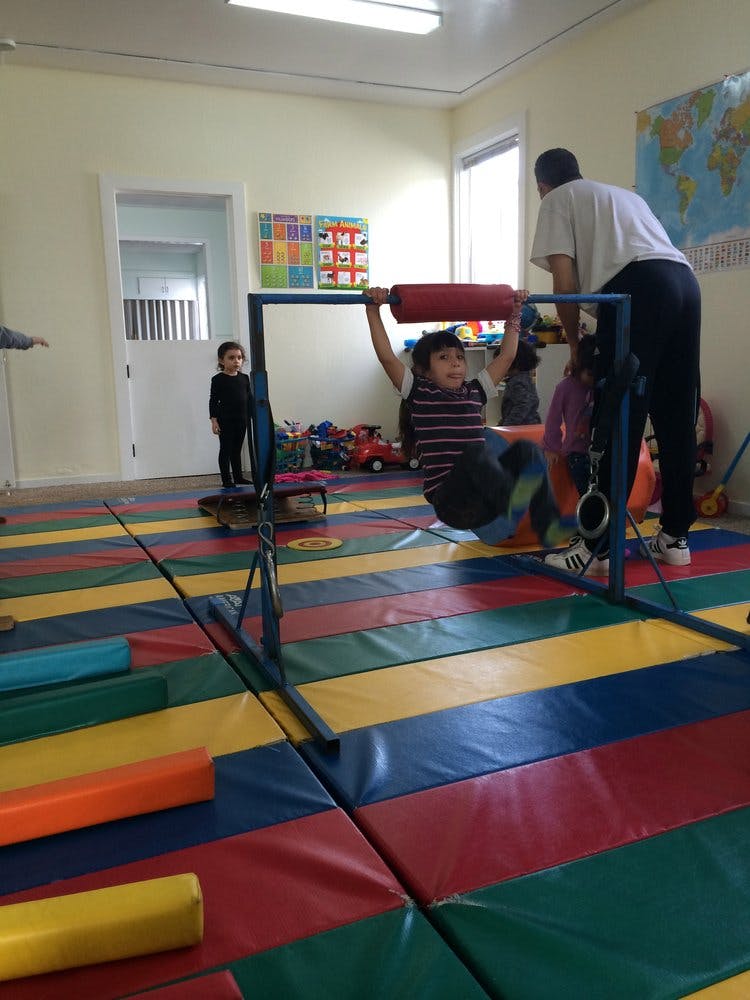 Child hanging from a bar in a room with colorful floor mats