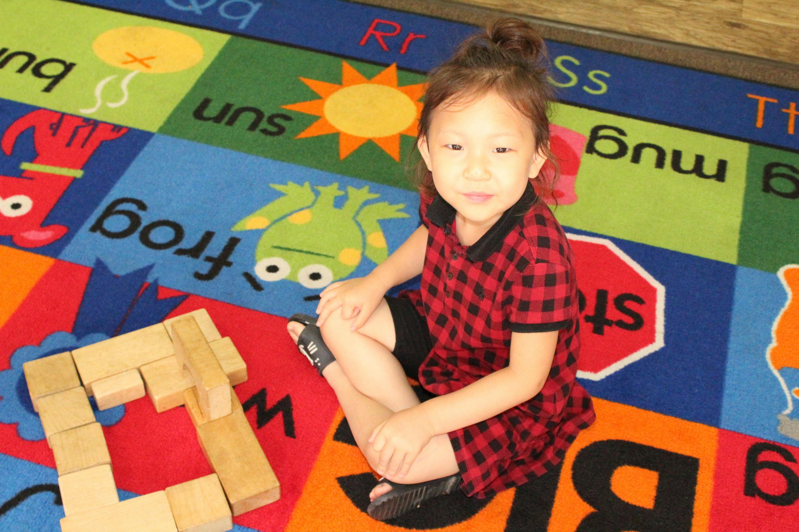 Child sitting on an alphabet rug with wooden blocks