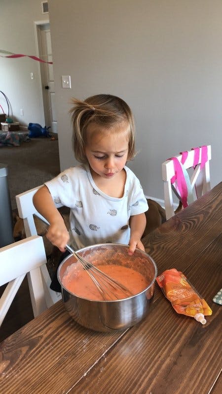 Child whisking batter in a bowl on a wooden table